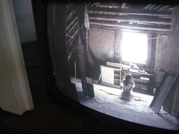 Most of the image is filled with a black and white screen of small television set. The image on the screen depicts a dusty attic and small white figure.