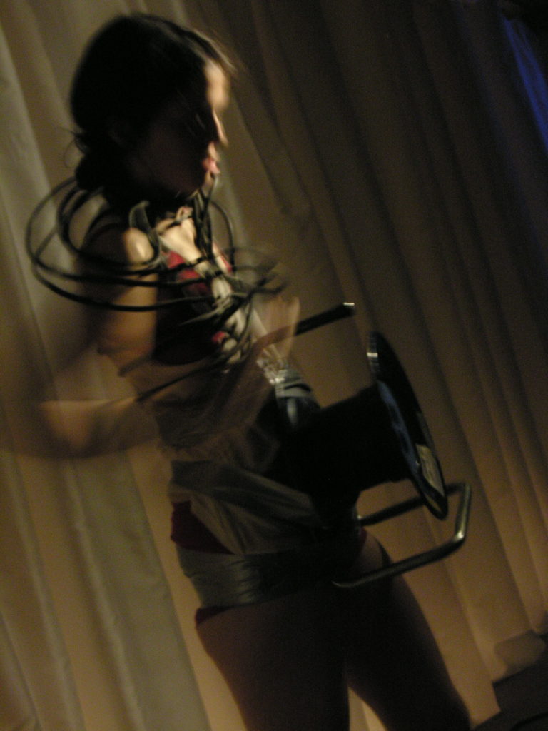 A figure with a extension cord drum wrapped around her. Her arms are moving and blurry and the perspective is slightly tilted.